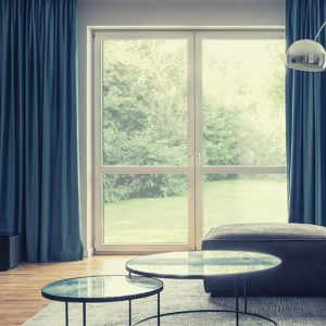 Deep blue motorized curtains framing wide glass doors beside a blue living-room sofa.